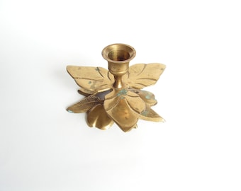 Puede incluir: Un candelero de metal dorado con forma de mariposa con detalles intrincados. El candelero tiene un solo hueco para la vela en el centro.