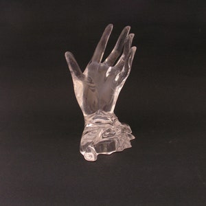 May include: A clear glass hand sculpture with an open palm, designed to hold rings or other small items.