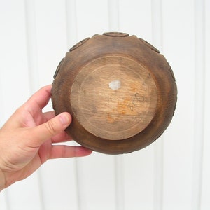 May include: A dark brown wooden bowl with a carved design around the rim. The bowl is empty and has a white sticker on the bottom.