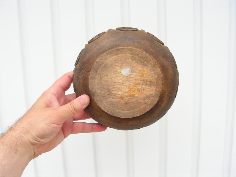 May include: A dark brown wooden bowl with a carved design around the rim. The bowl is empty and has a white sticker on the bottom.