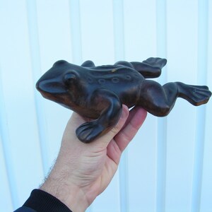 May include: A dark brown wooden frog figurine with a textured surface. The frog is posed in a jumping position with its legs outstretched.