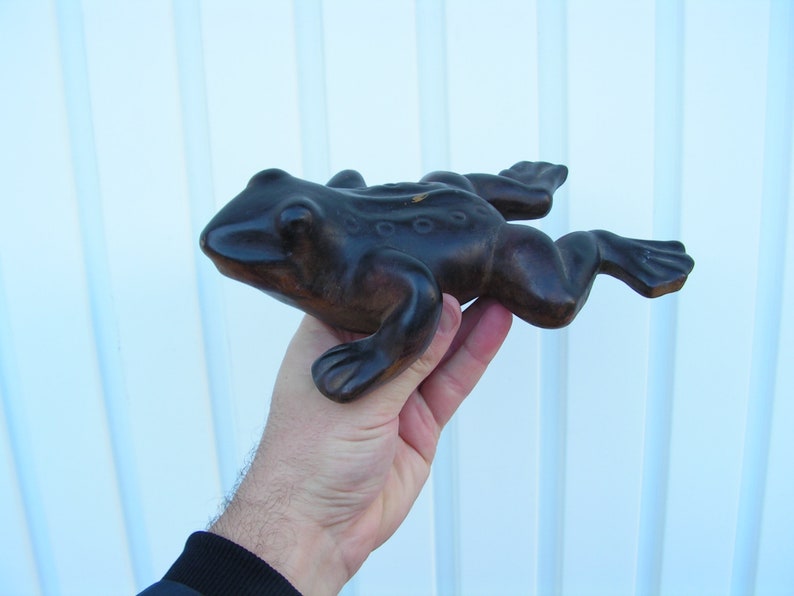 May include: A dark brown wooden frog figurine with a textured surface. The frog is posed in a jumping position with its legs outstretched.