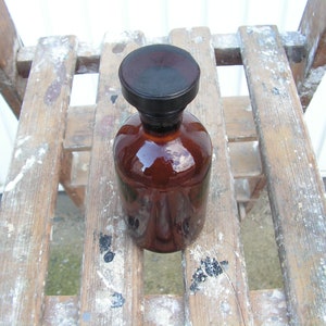May include: A brown glass bottle with a black lid, sitting on a wooden surface with white paint splatters.
