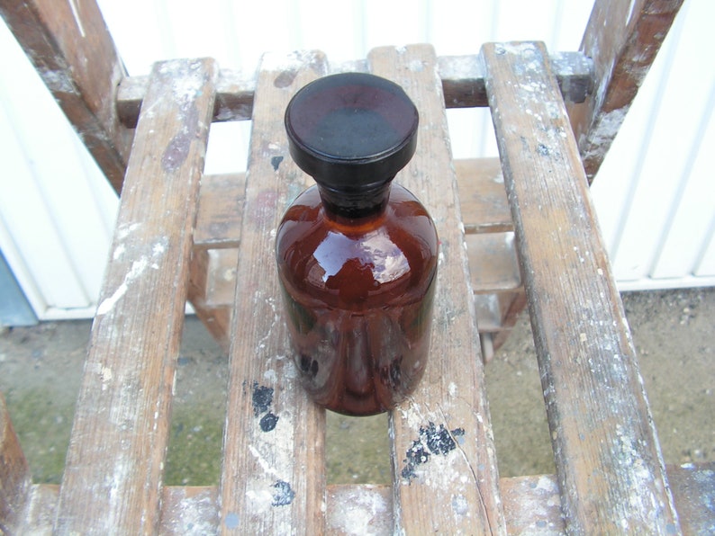 May include: A brown glass bottle with a black lid, sitting on a wooden surface with white paint splatters.