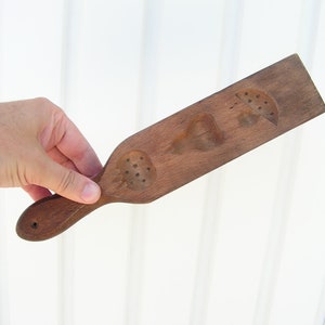 May include: A wooden mold for making cookies or pastries. The mold has three different shapes: a heart, a leaf, and a circle with dots. The mold has a handle on the side.