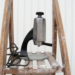 May include: A silver and black espresso maker with a black handle and a cord. The maker is sitting on a wooden shelf.