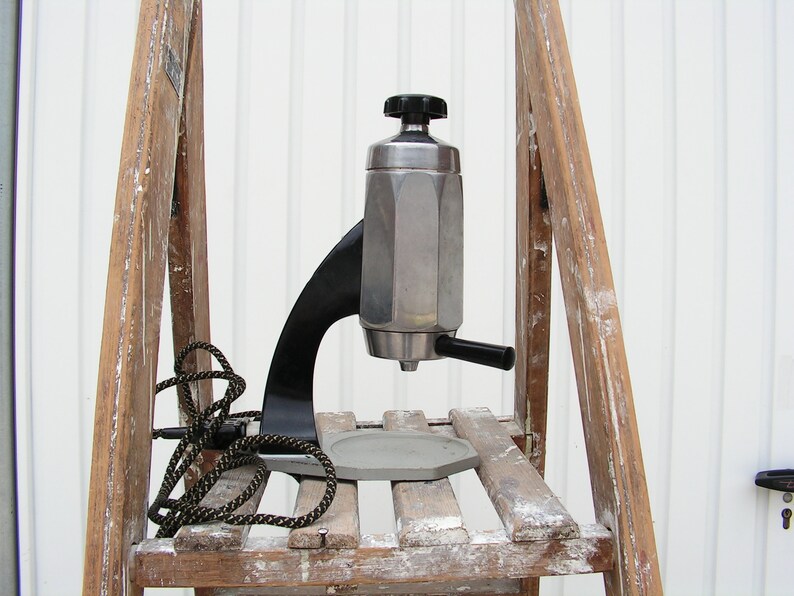 May include: A silver and black espresso maker with a black handle and a cord. The maker is sitting on a wooden shelf.