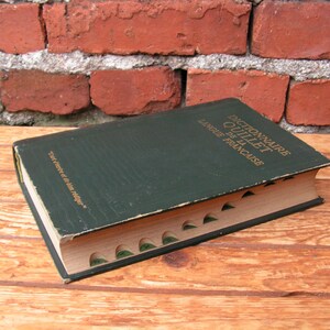 May include: A vintage green hardcover book titled "Dictionnaire Quillet de la Langue Fran&ccedil;aise" with gold lettering. The book has a worn appearance and is open to show the interior pages. The book is on a wooden surface.