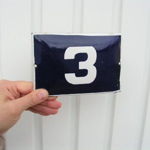 May include: A blue enamel house number sign with white painted number "3" on a white background.
