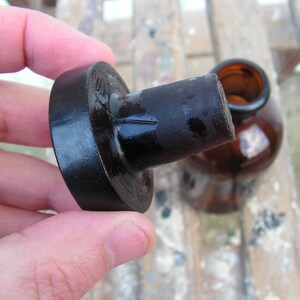 May include: A black glass bottle stopper with a round, flat top. The stopper is made of dark glass and has a smooth, shiny finish.