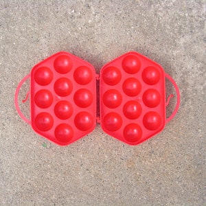 May include: A red plastic egg carton with 18 compartments, open and ready to hold eggs.