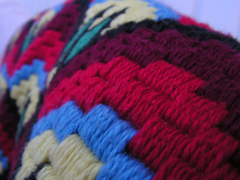 May include: Close-up of a colorful, textured textile with a geometric pattern. The design features vibrant red, blue, yellow, and green yarn, creating a visually appealing and intricate design. The fabric appears to be hand-stitched or crocheted, showcasing a handcrafted aesthetic.