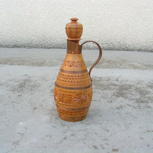 K&ouml;nnte beinhalten: Eine Holzflasche mit einem geschnitzten Design und einem kupfernen Oberteil und Griff. Die Flasche ist braun und hat einen traditionellen Volksstil.