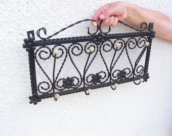 Op de afbeelding: Zwarte metalen wandhaak met decoratieve krulwerk en witte kunststofknoppen. De haak heeft vijf haken.