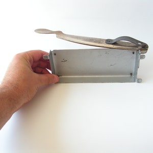 May include: A vintage metal food cutter with a silver finish and a black handle. The cutter is open and ready to use.