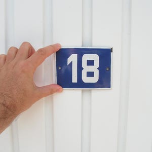 Könnte beinhalten: Ein blaues und weißes Email-Hausnummernschild mit der Nummer 18 auf weißem Hintergrund.