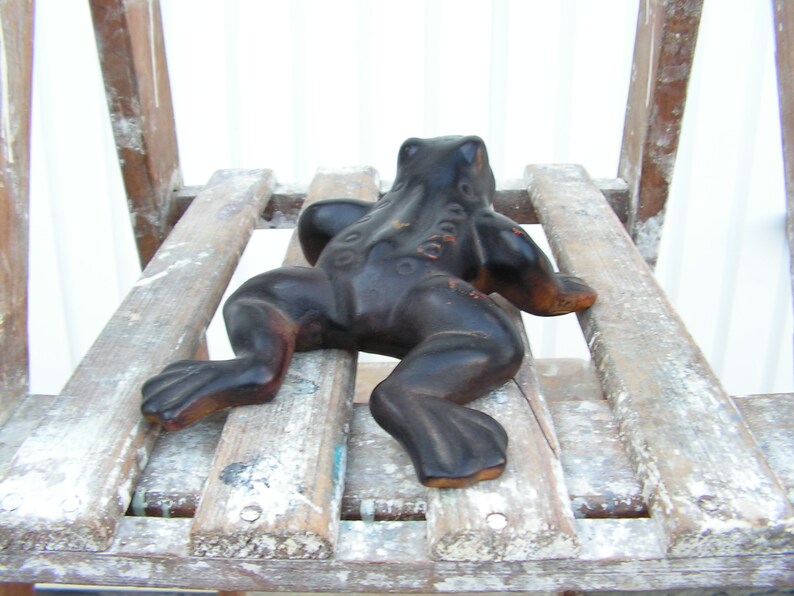 May include: A black frog figurine sitting on a wooden chair. The frog is made of a smooth, dark material and has a textured surface. The chair is made of wood and has a white paint finish.