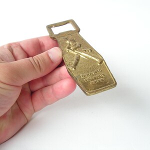 May include: A gold-coloured bottle opener with a raised image of a baseball player and the text "Boston Red Sox" on the front.