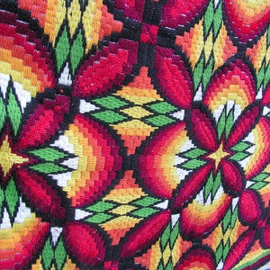 May include: Close-up of a colorful, embroidered textile with a repeating floral pattern. The design features red, orange, yellow, green, and black threads, creating a vibrant and textured surface. The textile appears to be a decorative piece.