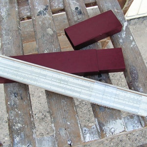 Może przedstawiać: Wzorcowa suwmiarka w burgundowym etui. Suwmiarka wykonana jest z białego plastiku i posiada różne skale i oznaczenia. Etui wykonane jest z twardego, burgundowego plastiku i posiada zatrzask.