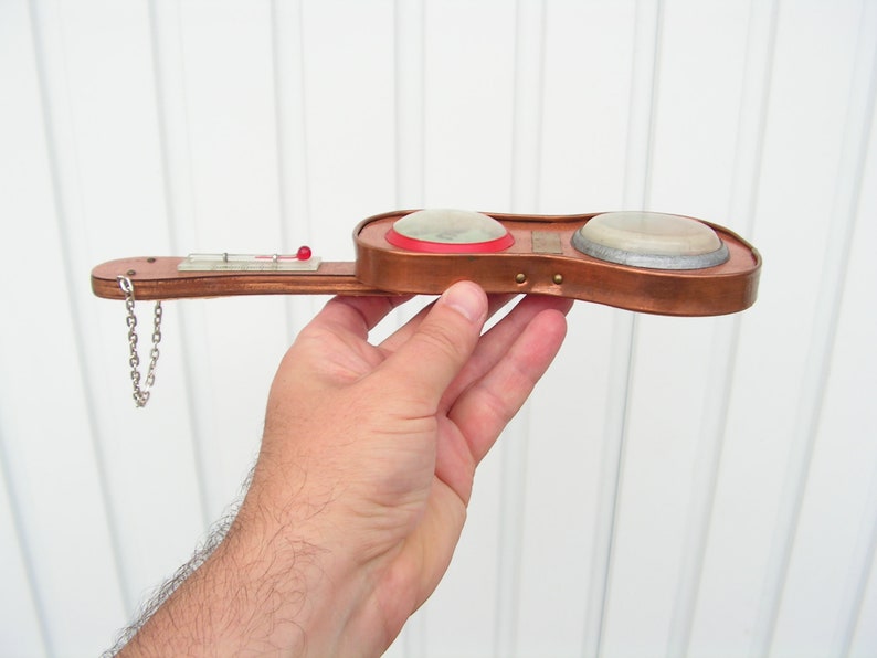 May include: A small, copper-colored, guitar-shaped object with two round, white, and silver-colored dials. The object has a small, red button on the top and a silver chain attached to the bottom.
