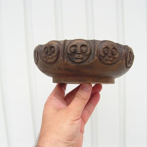 May include: A brown wooden bowl with a carved design of faces around the rim.