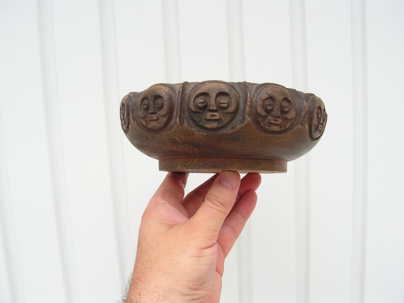 May include: A brown wooden bowl with a carved design of faces around the rim.