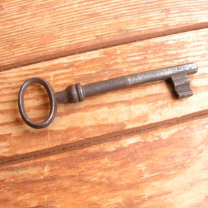 May include: An antique, rusty metal key with a large oval-shaped bow. The key is lying on a wooden surface.