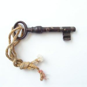 May include: An antique key with a dark, aged metal finish. The key is attached to a twisted rope with tan and white threads. The key's design includes a circular handle and a rectangular bit.