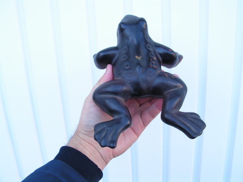 May include: A black cast iron frog figurine. The frog is sitting on its hind legs with its front legs outstretched. The frog has a textured surface and a detailed design.