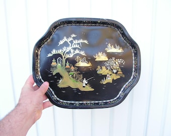 Può includere: Un vassoio in metallo nero con un design dipinto in oro e bianco di un paesaggio cinese. Il vassoio ha un bordo a festoni ed è decorato con un bordo dorato.
