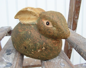 Könnte beinhalten: Eine Keramik-Hasenfigur mit einer grün-braunen, gesprenkelten Glasur. Der Hase hat ein einzelnes, großes, schwarzes Auge und ein schlaffes, braunes Ohr.