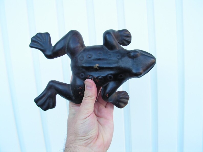 May include: A black cast iron frog doorstop with a textured surface. The frog is in a leaping pose with its legs outstretched.