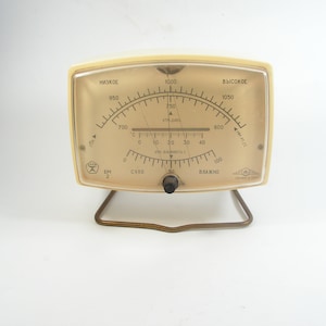 Puede incluir: Un barómetro analógico vintage blanco con un soporte de metal dorado. La cara del barómetro tiene una aguja negra y marcas para "низкое" (bajo) y "высокое" (alto) en escritura cirílica.