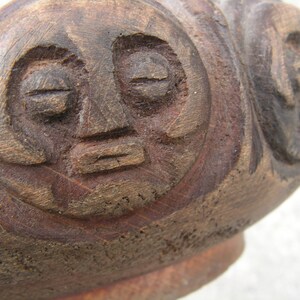 May include: A close-up of a wooden carving of a face with closed eyes and a carved mouth. The carving is dark brown and has a rough texture.