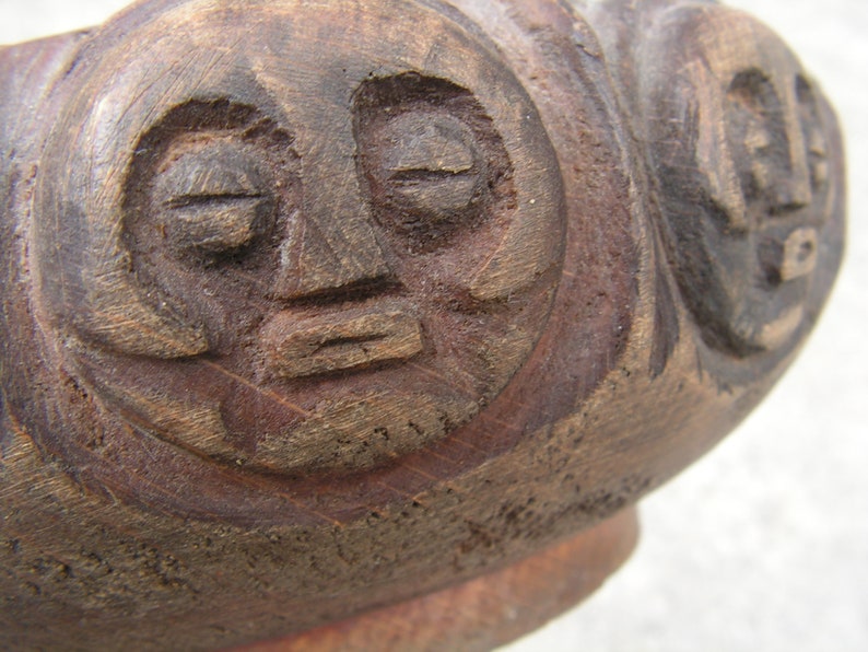 May include: A close-up of a wooden carving of a face with closed eyes and a carved mouth. The carving is dark brown and has a rough texture.