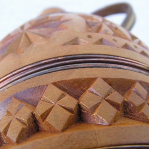 K&ouml;nnte beinhalten: Ein Holzbeh&auml;lter mit einem geschnitzten Design und einem Kupferband um die Oberseite. Der Beh&auml;lter hat einen Griff und ist aus hellem braunem Holz gefertigt.