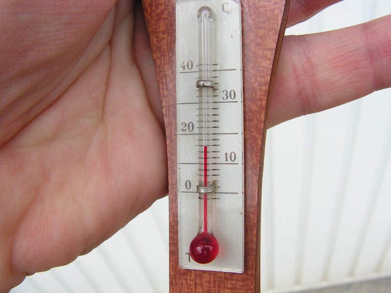 May include: A wooden thermometer with a red liquid inside. The thermometer is marked in Celsius and shows a temperature of 5 degrees.
