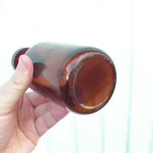 May include: A brown glass bottle with a wide mouth, viewed from the bottom. The bottle is empty and has a slightly cloudy appearance.