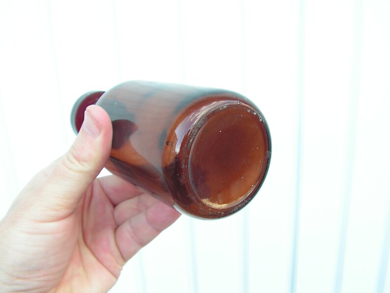 May include: A brown glass bottle with a wide mouth, viewed from the bottom. The bottle is empty and has a slightly cloudy appearance.