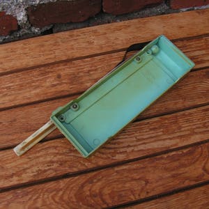 May include: A light green plastic box with a white plastic handle. The box has several small holes on the top and is sitting on a wooden surface.