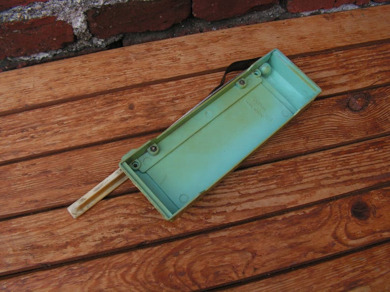 May include: A light green plastic box with a white plastic handle. The box has several small holes on the top and is sitting on a wooden surface.