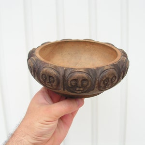 May include: A brown wooden bowl with a carved design of faces around the rim.