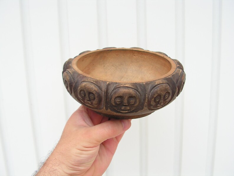 May include: A brown wooden bowl with a carved design of faces around the rim.