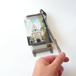 May include: A vintage metal photo cutter with a silver finish and a brown handle. A photo of a church with a tall spire is in the cutter.