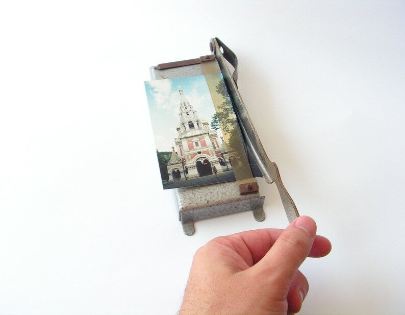May include: A vintage metal photo cutter with a silver finish and a brown handle. A photo of a church with a tall spire is in the cutter.