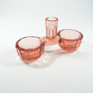 Peut inclure: Un ensemble de salière et poivrière en verre rose avec un distributeur central. Les salières ont un design facetté et le distributeur a une forme cylindrique.