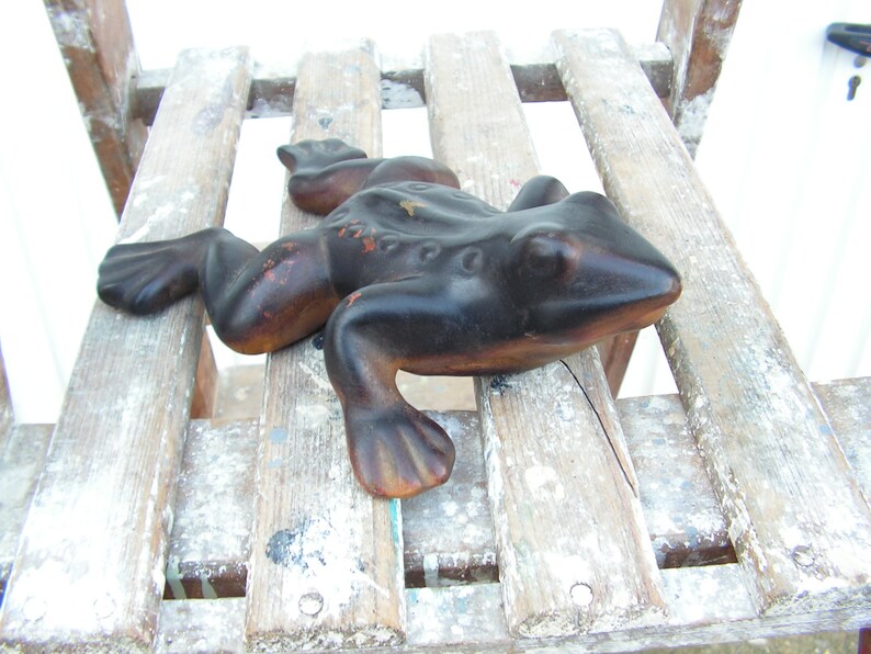 May include: A black frog figurine with a textured surface, sitting on a wooden slatted surface.