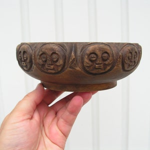 May include: A dark brown wooden bowl with a carved design of faces around the rim.