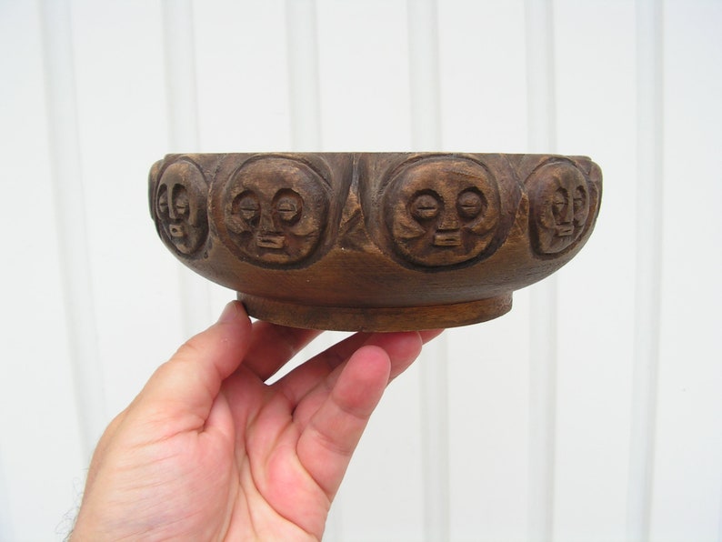 May include: A dark brown wooden bowl with a carved design of faces around the rim.